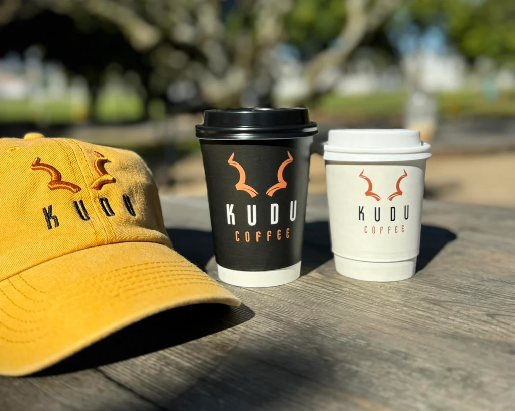 KUDU Coffee branded yellow cap with black and white branded takeaway cups